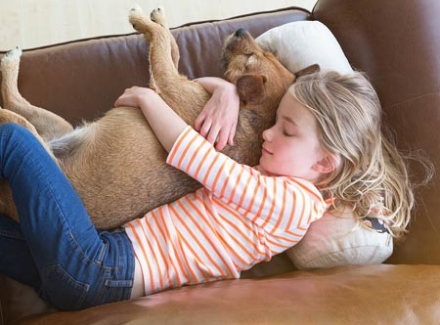 little girl laying on leather couch hugging dog